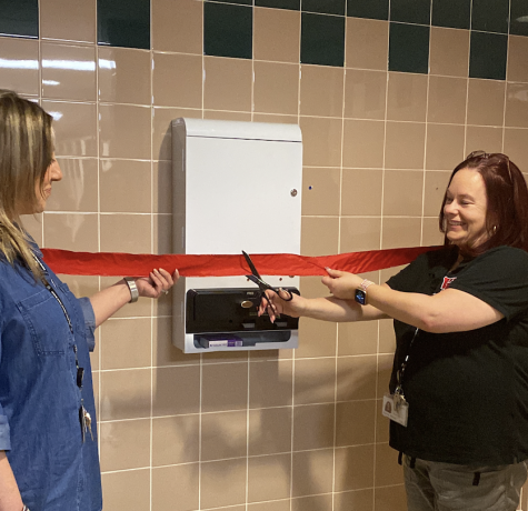 Nurse Karen Kinsey and Shara Lekston, secretary to the director of Building & Grounds, formally cut the ribbon on the menstrual products dispenser Dec. 6 in a school bathroom. The Womens Empowerment Club held a ribbon cutting for the new dispensers on Dec. 6.